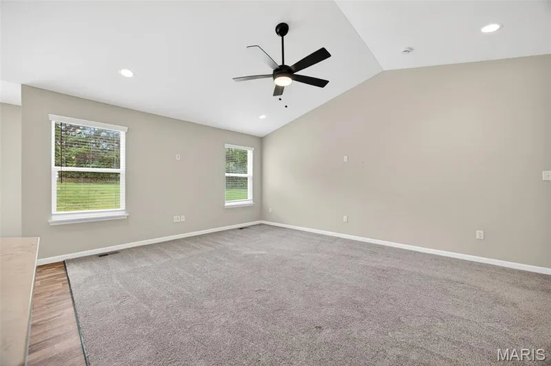 Spacious room featuring vaulted ceilings, a contemporary ceiling fan, recessed lighting, two large windows, and neutral carpeting — 112 Creek Haven Court, Lake St. Louis, MO 63367