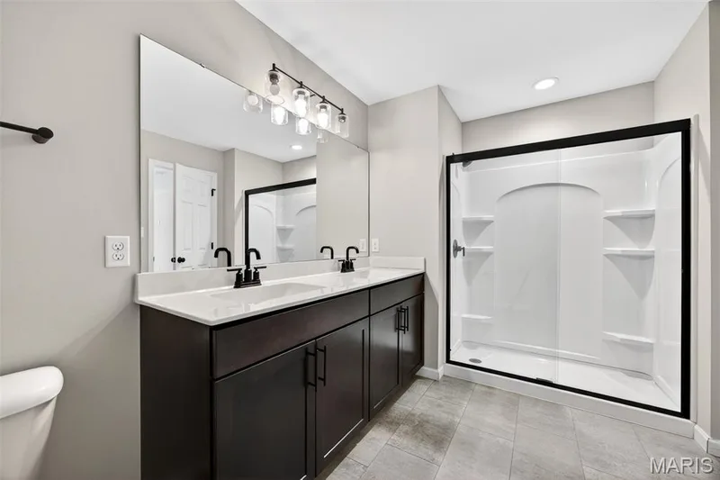 Bathroom featuring a dual vanity with dark wood-finish cabinetry, white countertop, and matte black fixtures — 112 Creek Haven Court, Lake St. Louis, MO 63367