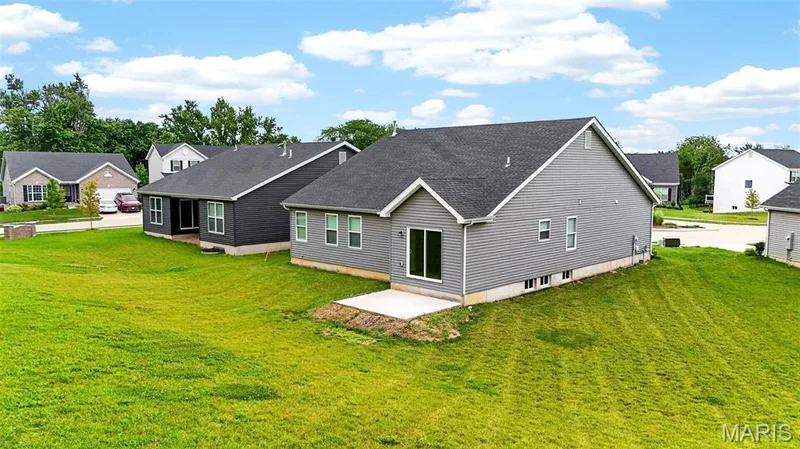Spacious backyard featuring a large concrete patio, sliding glass door access, ample green space, and a neutral-toned siding exterior — 112 Creek Haven Court, Lake St. Louis, MO 63367
