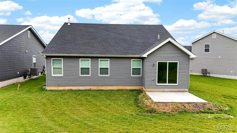 Rear exterior featuring gray horizontal siding, a dark shingle roof, a concrete patio, and a sliding glass door — 112 Creek Haven Court, Lake St. Louis, MO 63367