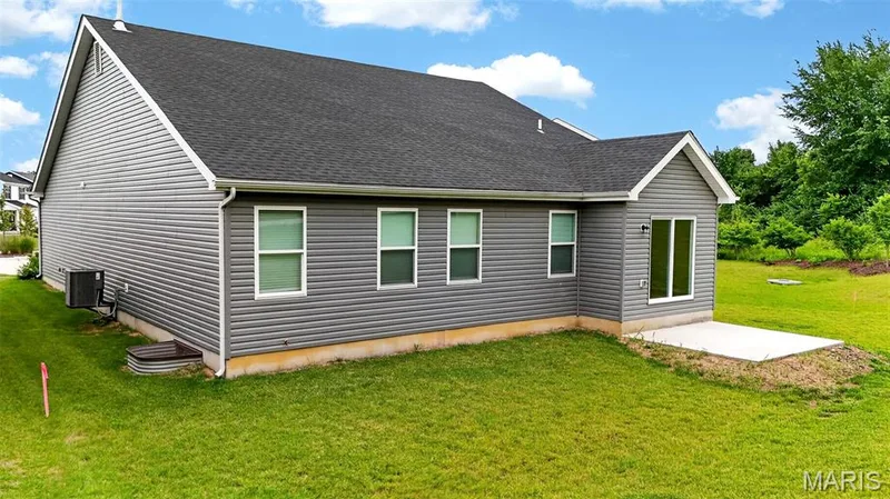 Rear exterior showcasing gray horizontal siding, a dark gray shingle roof, multiple windows, a sliding glass door, and a concrete patio — 112 Creek Haven Court, Lake St. Louis, MO 63367