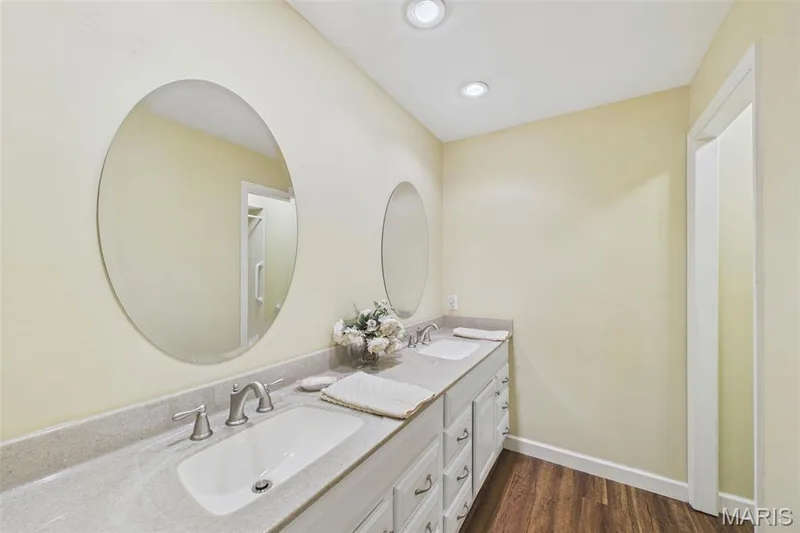 Updated bath with white cabinets, wood-like flooring and hard-surface counters. and double sinks.  Private tub/shower & commode. — 1525 Hampton Hall Drive #22, Chesterfield, MO 63017