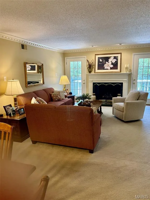 Living room featuring a fireplace with a white mantel, two sets of French doors, crown molding, and carpeted flooring — 1525 Hampton Hall Drive #22, Chesterfield, MO 63017