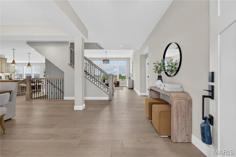 Expansive open-concept entry featuring wood-finish flooring, a contemporary staircase with dark iron balusters, and abundant natural light from large windows — 26 Valor Way, O'Fallon, MO 63385