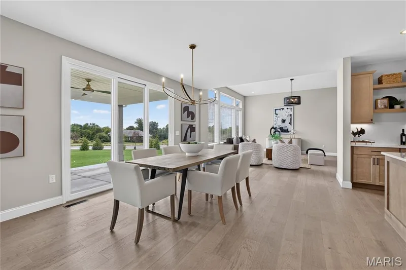 Open-concept living area with wood-finish flooring, a contemporary chandelier, and large sliding glass doors leading to an outdoor covered patio — 26 Valor Way, O'Fallon, MO 63385