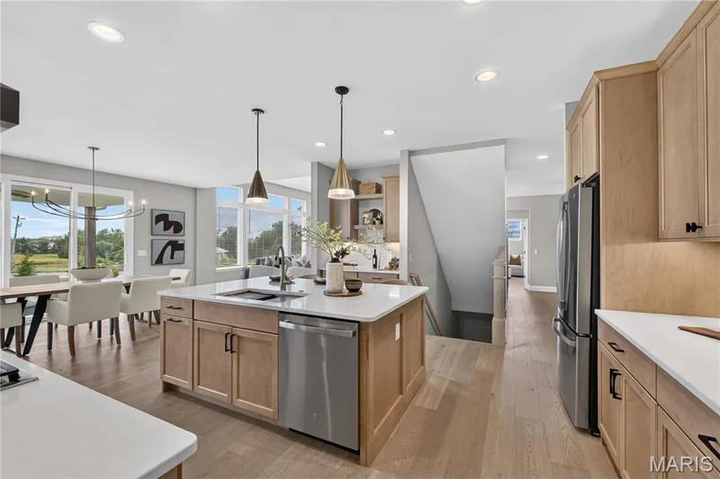 Open-concept kitchen and dining area featuring light wood-finish cabinetry, stainless steel appliances, a center island with sink, and recessed lighting — 26 Valor Way, O'Fallon, MO 63385
