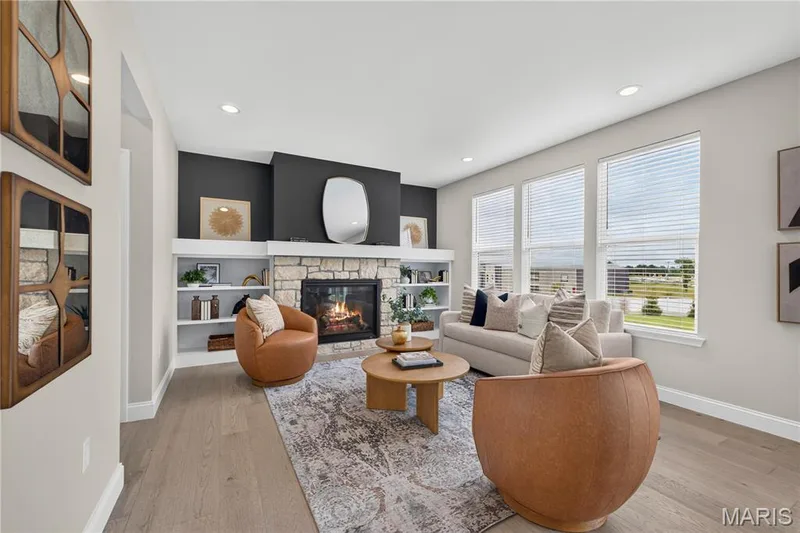 Hearth room featuring a  fireplace with a mantle, recessed lighting, built-in shelving, wood-finish flooring, and multiple windows — 26 Valor Way, O'Fallon, MO 63385