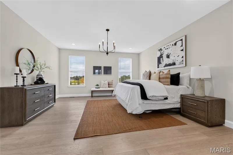 Main floor Primary Bedroom featuring wood-finish flooring, light neutral wall tones, and multiple windows — 26 Valor Way, O'Fallon, MO 63385