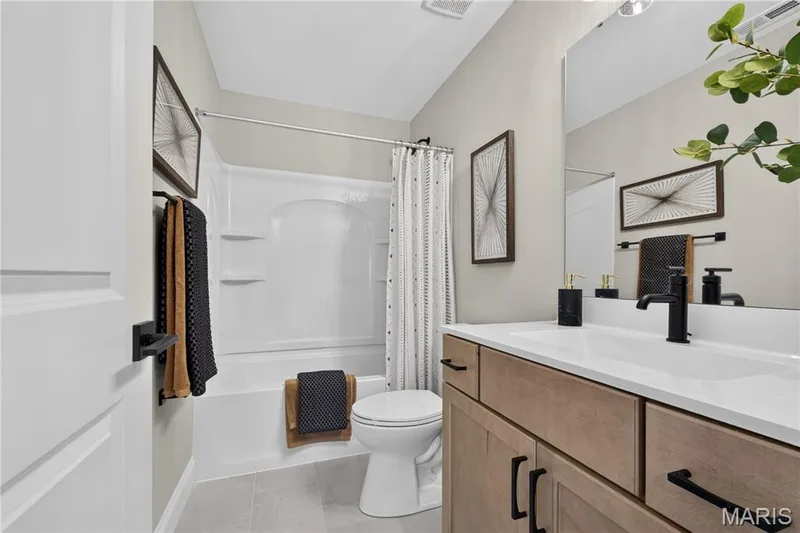 Second floor full bathroom featuring a built-in tub and shower combination, a single vanity with a white countertop, wood-finish cabinetry, and matte black fixtures — 26 Valor Way, O'Fallon, MO 63385