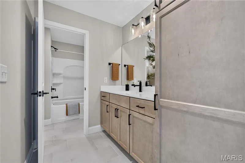 Jack and Jill Bathroom with seperate vanity with quartz countertop, light wood-finish cabinetry, and black hardware — 26 Valor Way, O'Fallon, MO 63385