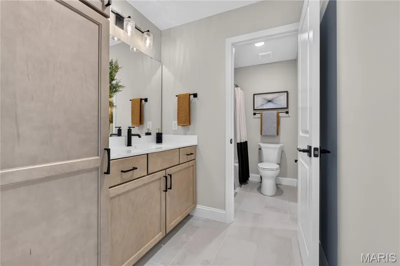 Jack and Jill Bathroom with seperate  vanity with light wood-finish cabinetry, white countertop, and matte black fixtures — 26 Valor Way, O'Fallon, MO 63385