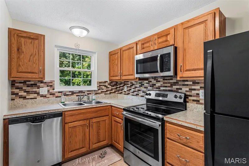 Kitchen featuring wood cabinetry, stainless steel dishwasher, stainless steel microwave, and mosaic tile backsplash — 1511 Hampton Hall Drive #10, Chesterfield, MO 63017