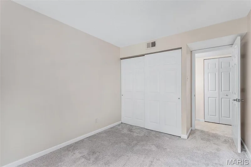 Neutral-toned walls, light gray carpeting, and white bi-fold closet doors — 1511 Hampton Hall Drive #10, Chesterfield, MO 63017