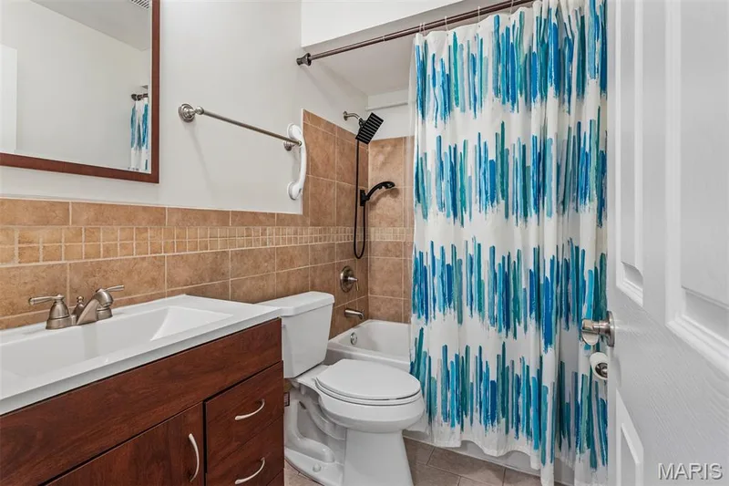 Bathroom featuring a wood-finish vanity with an integrated sink, brushed nickel faucet, and a tiled shower surround — 1511 Hampton Hall Drive #10, Chesterfield, MO 63017