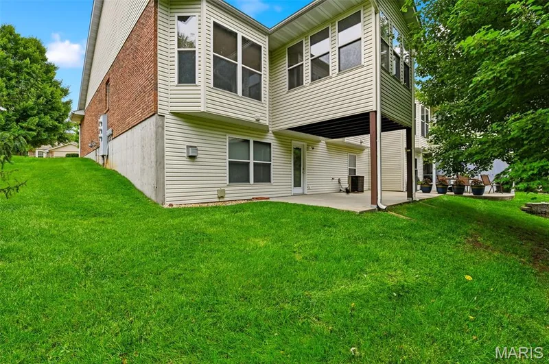 Rear exterior showcasing a brick and siding facade with a ground-level patio, an upper-level covered deck, and a bay window feature — 3515 Truman Terrace Drive #65, St Charles, MO 63301