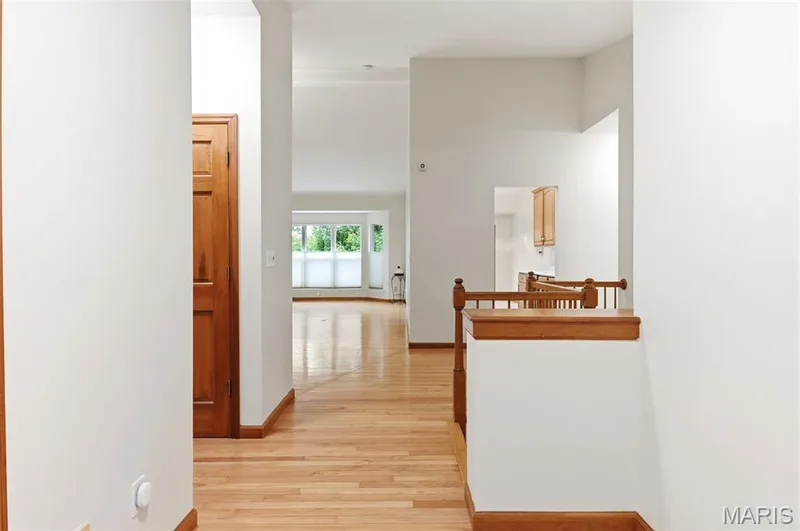 Interior hallway featuring light wood-finish flooring, white wall paint, and natural wood trim — 3515 Truman Terrace Drive #65, St Charles, MO 63301