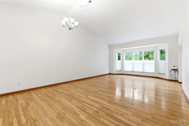 Spacious room featuring vaulted ceilings, polished wood-finish flooring, and a multi-pane bay window with privacy blinds — 3515 Truman Terrace Drive #65, St Charles, MO 63301