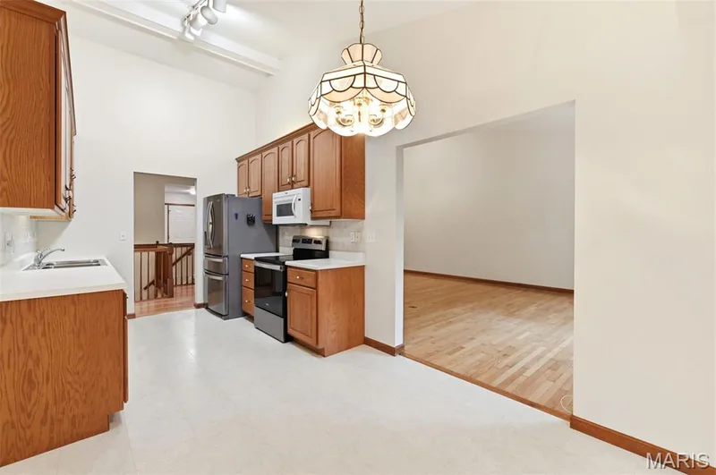 Kitchen featuring vaulted ceilings with track lighting, wood cabinetry, white countertops, and white tile flooring — 3515 Truman Terrace Drive #65, St Charles, MO 63301