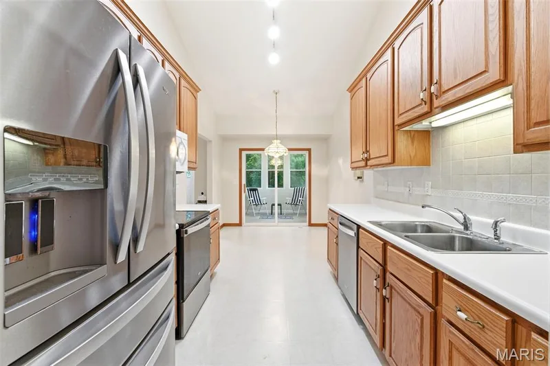 Kitchen featuring wood cabinetry, stainless steel appliances, white countertops, and a tile backsplash — 3515 Truman Terrace Drive #65, St Charles, MO 63301