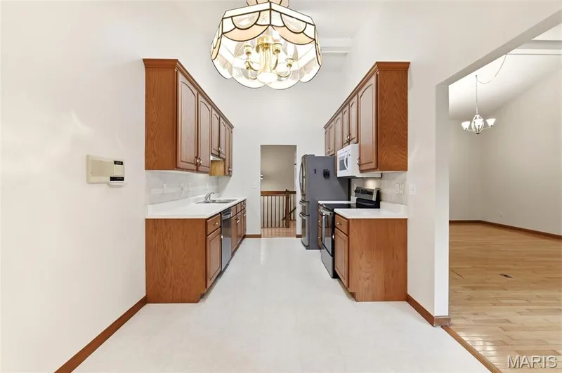 Galley kitchen featuring wood cabinetry, white countertops, and a tile backsplash — 3515 Truman Terrace Drive #65, St Charles, MO 63301