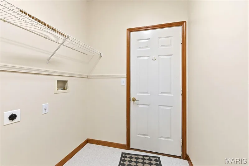 Laundry area with light-toned walls, white wire shelving, a white paneled door with wood-finish trim, and light-colored speckled flooring — 3515 Truman Terrace Drive #65, St Charles, MO 63301