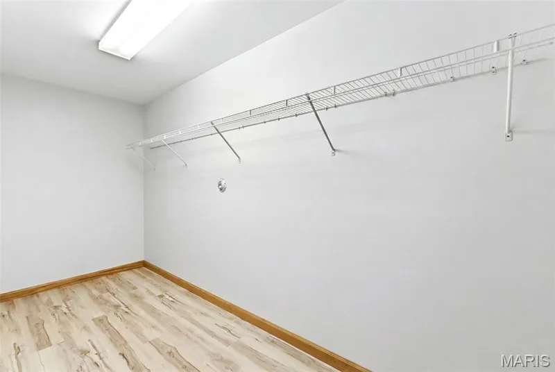 Spacious utility room featuring durable wood-finish flooring, a fluorescent ceiling light fixture, white walls, and a convenient wire shelving system — 3515 Truman Terrace Drive #65, St Charles, MO 63301