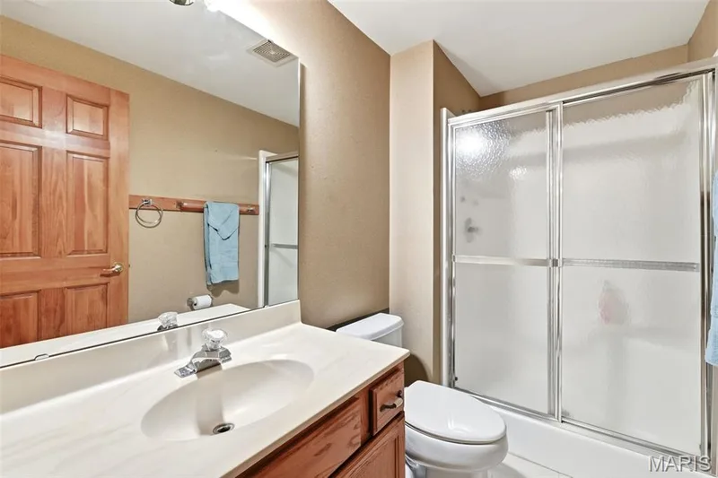 Full bathroom featuring a vanity with an integrated sink, a rectangular mirror, a shower-tub combination with sliding frosted glass doors, and a toilet — 3515 Truman Terrace Drive #65, St Charles, MO 63301