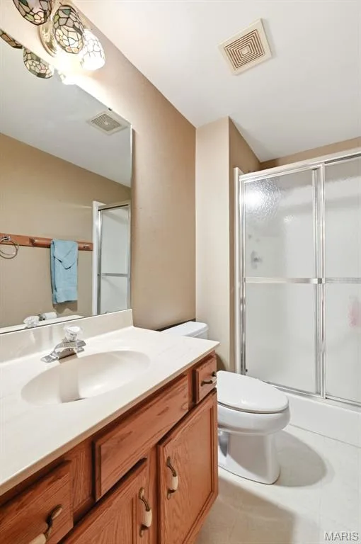 Full bathroom featuring a wood-finish vanity with an integrated sink, a mirrored wall, and a shower with sliding glass doors — 3515 Truman Terrace Drive #65, St Charles, MO 63301