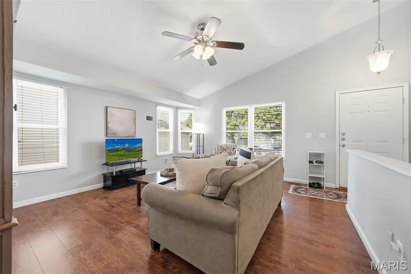 Living area with vaulted ceiling, wood-finish flooring, multiple windows providing natural light, and a ceiling fan with integrated lighting — 2510 Balaji Court, Wildwood, MO 63011