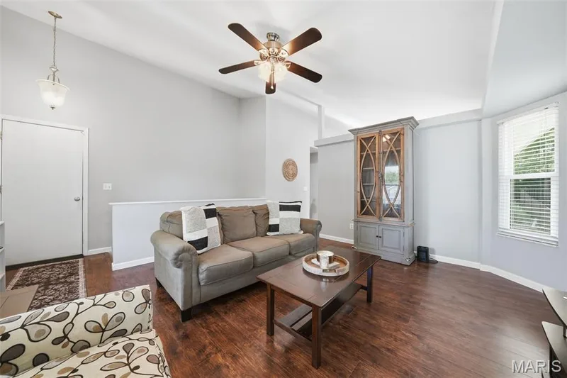 Spacious living area featuring vaulted ceilings, wood-finish flooring, a ceiling fan with integrated lighting, and a bay window with blinds — 2510 Balaji Court, Wildwood, MO 63011