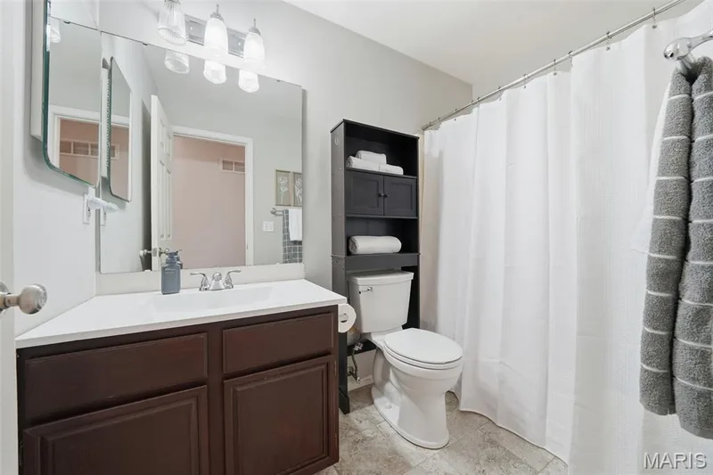 Bathroom featuring a wood-finish vanity with a white countertop, large mirror, chrome fixtures, and tile flooring — 2510 Balaji Court, Wildwood, MO 63011
