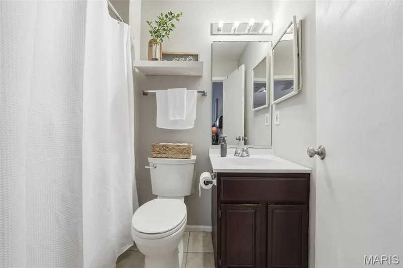 Bathroom featuring a dark wood-finish vanity with a white countertop and integrated sink, a wall-mounted mirror, and a white toilet — 2510 Balaji Court, Wildwood, MO 63011
