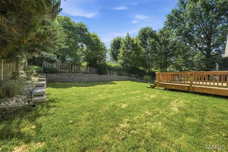 Spacious backyard featuring a large wooden deck, expansive lawn, mature perimeter trees, stone retaining walls, and concrete stepping stones — 2510 Balaji Court, Wildwood, MO 63011