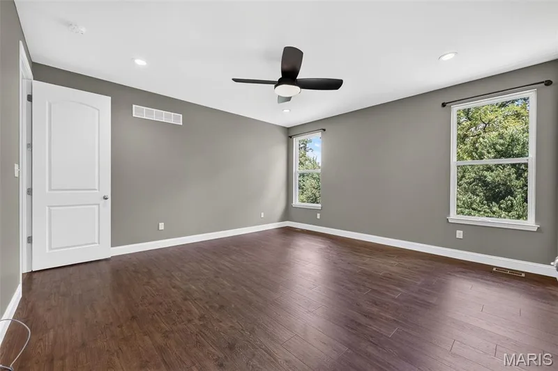 Spacious room featuring wood-finish flooring, two windows with white trim, a ceiling fan, recessed lighting, and a white paneled door — 401 Hamlet Court, O'Fallon, MO 63367