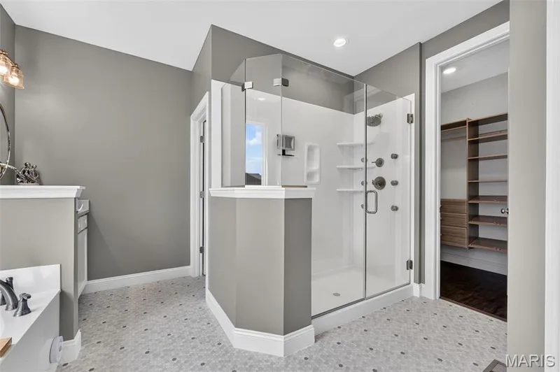Glass-enclosed shower with multiple spray features, hexagon tile flooring, built-in shelving, and a vanity with a dark countertop — 401 Hamlet Court, O'Fallon, MO 63367