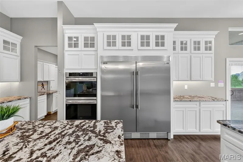 Stainless steel built-in double oven, paneled cabinetry, stainless steel side-by-side refrigerator, wood-finish flooring, and granite countertops — 401 Hamlet Court, O'Fallon, MO 63367