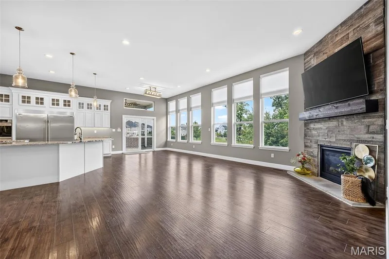 Open-concept living space with dark wood-finish flooring, a stone-clad fireplace, and an array of large windows — 401 Hamlet Court, O'Fallon, MO 63367