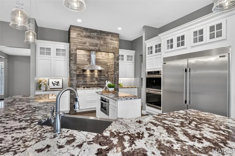 Gourmet kitchen featuring granite countertops, stainless steel appliances, white cabinetry, and a stacked stone accent wall with range hood — 401 Hamlet Court, O'Fallon, MO 63367