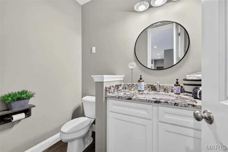 Bathroom featuring a vanity with white cabinetry, a stone countertop, an undermount sink, a circular mirror, and a three-light fixture — 401 Hamlet Court, O'Fallon, MO 63367