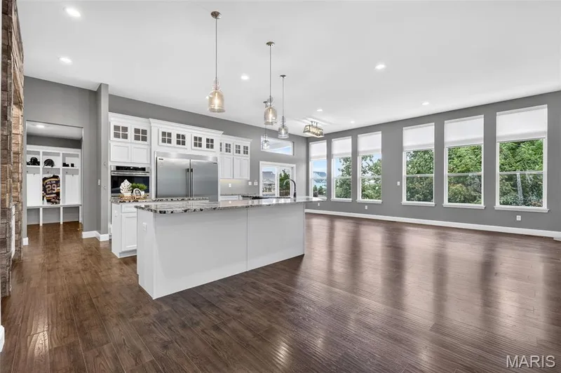 Spacious open-concept living area featuring wood-finish flooring, white cabinetry, a kitchen island with a stone-finish countertop, and multiple large windows — 401 Hamlet Court, O'Fallon, MO 63367