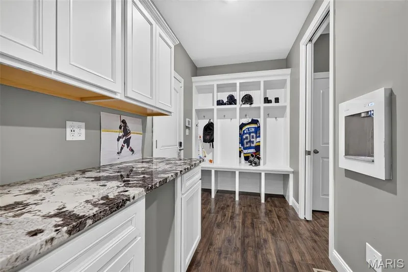 Built-in cabinetry with a stone countertop, overhead white shaker-style cabinets, wood-finish flooring, and a built-in bench with storage cubbies — 401 Hamlet Court, O'Fallon, MO 63367