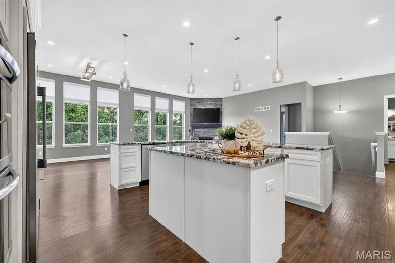 Spacious interior with rich wood-finish flooring, white cabinetry, and a substantial island featuring a granite-style countertop — 401 Hamlet Court, O'Fallon, MO 63367
