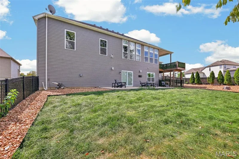 Expansive backyard featuring a manicured lawn, a full wooden deck, a ground-level patio, and a privacy fence — 401 Hamlet Court, O'Fallon, MO 63367