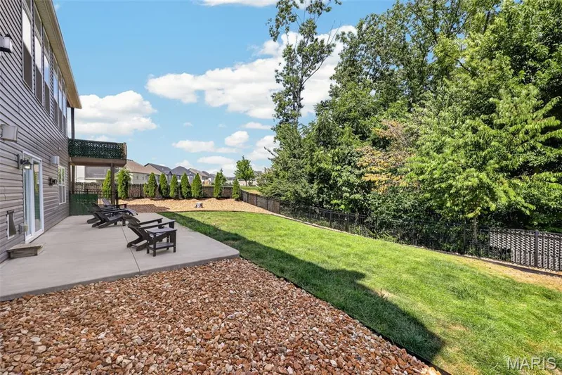 Expansive backyard featuring a concrete patio, decorative gravel, a grassy area, and mature trees — 401 Hamlet Court, O'Fallon, MO 63367