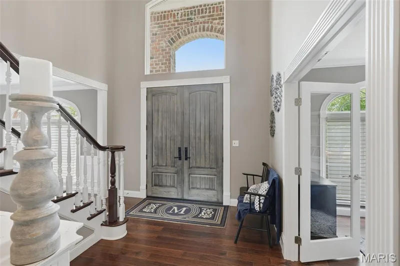 Foyer featuring wood-finish flooring, a grand staircase with white balusters and dark wood handrails, and a double-door entry with an arched transom window — 1660 Garden Valley Court, Wildwood, MO 63038
