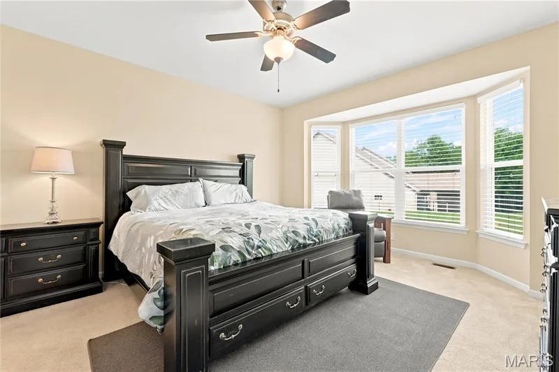 Spacious primary bedroom featuring a bay window, ceiling fan, and neutral carpet flooring — 226 City Gate Lane, St Charles, MO 63303