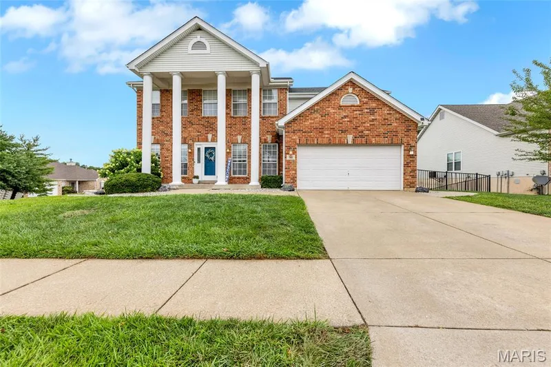 Brick facade residence featuring a prominent portico with white columns, a two-car garage, and an expansive concrete driveway — 501 Oxborough Court, Cottleville, MO 63376