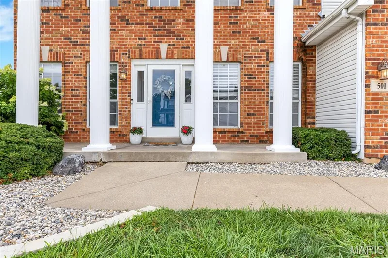 Classic brick with a serious glow-up. Bold white columns frame the main entry, turning a simple front door into a total statement piece. — 501 Oxborough Court, Cottleville, MO 63376
