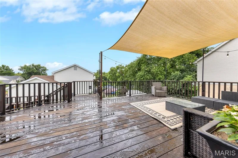 Expansive wooden deck featuring dark railings, a light-colored sun shade, and string lighting — 501 Oxborough Court, Cottleville, MO 63376