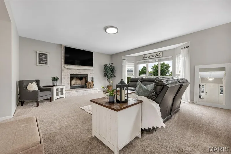 Living area featuring a brick-surround fireplace, bay windows, light neutral wall colors, recessed lighting, and carpeted flooring — 501 Oxborough Court, Cottleville, MO 63376
